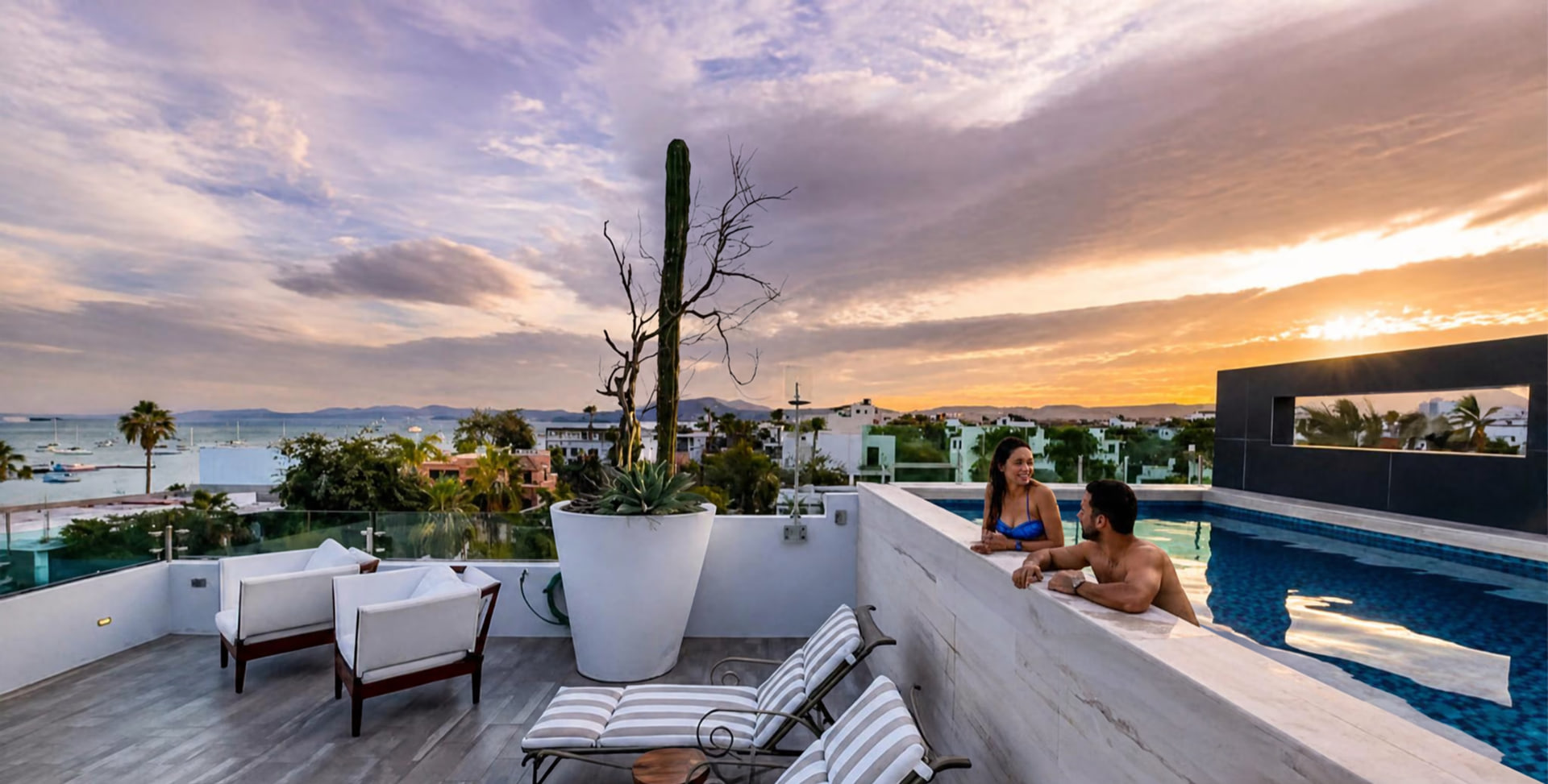 Una pareja en la alberca climatizada del rooftop de Casa Altamar, con la bahía de La Paz y el atardecer al fondo